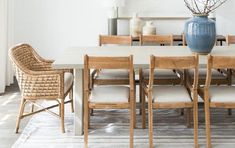 a dining room table with chairs and a vase on it's centerpiece, in front of a white wall