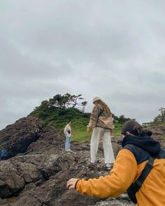 two people standing on top of a rocky beach next to the ocean and one person flying a kite