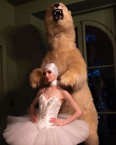 a woman standing next to a giant teddy bear in a tutu and white dress