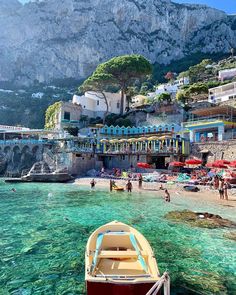 a boat is sitting in the clear water near some buildings and people on the beach