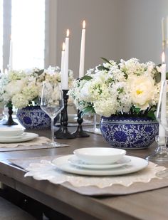 a dining table with white flowers and candles in blue vases on the centerpiece