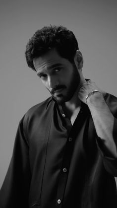 black and white photograph of a man adjusting his shirt in front of a gray background