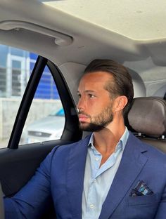 a man in a blue suit sitting in the back seat of a car looking at something