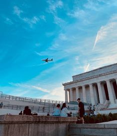 an airplane flying over the lincoln memorial with people sitting on the steps watching it fly by