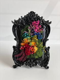 a black frame with flowers in it on a white tableclothed surface and the image is framed by an ornately decorated frame