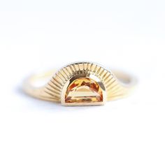 a yellow gold ring with an orange stone in the center on a white background,