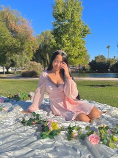 a woman in a pink dress sitting on a blanket talking on a cell phone with roses all around her