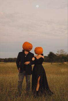 two people standing in a field with pumpkins on their heads looking at the sky