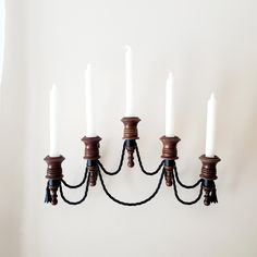 a wall mounted candle holder with five white candles on it's arms and four black cords