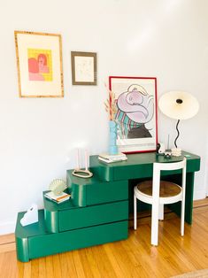 a green desk with two stools and a painting on the wall in front of it