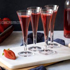 three glasses filled with liquid sitting on top of a cutting board next to strawberries