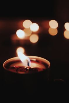 a lit candle is sitting in front of some blurred lights on a dark table top