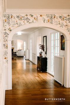 an archway leading into a living room with wood floors and white walls, decorated in floral wallpaper