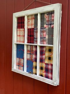 an old window is hung on the side of a red building with plaid fabric in it