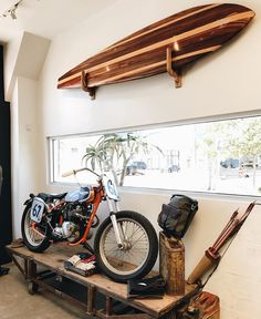 a motorcycle is parked next to a surfboard on a shelf in a room with other items