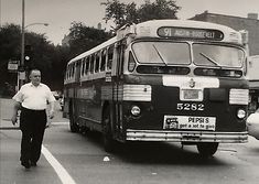 black and white photograph of a man walking across the street in front of a bus