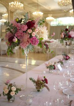 the table is set with wine glasses and flowers in vases on top of it