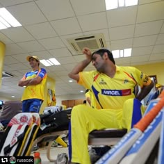 two men in yellow and blue uniforms sitting on benches with their hands behind their heads