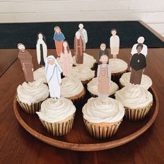 cupcakes with paper cutouts of people on them sitting on a wooden plate