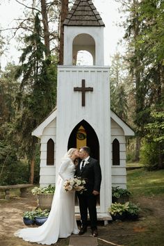 a bride and groom kissing in front of a small church with a cross on it