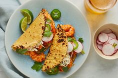 two fish tacos on a plate next to a cup of tea and sliced radishes