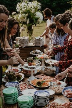 a group of people standing around a table filled with plates and bowls full of food