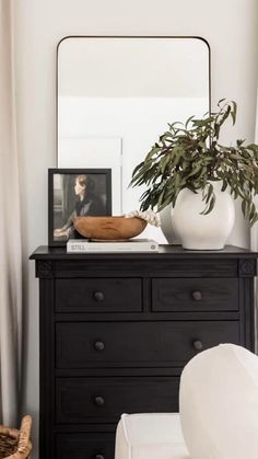 a black dresser with a mirror and potted plant on top in front of it