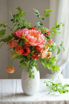 a white vase filled with lots of flowers on top of a table next to plants