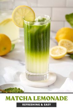 a tall glass filled with green liquid next to lemons