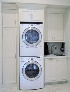 two washers and a dryer in a small room with white cabinets on the walls