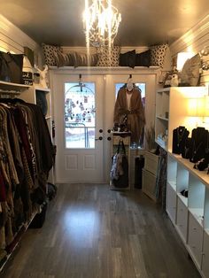 the inside of a clothing store with lots of clothes hanging on shelves and doors open