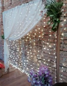 a brick wall with white lights on it and flowers in the corner next to it