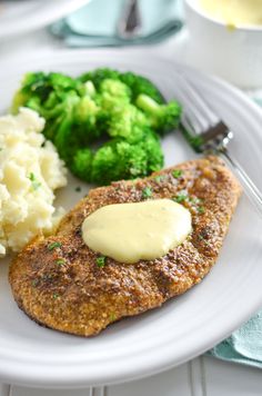 a white plate topped with meat covered in gravy next to mashed potatoes and broccoli