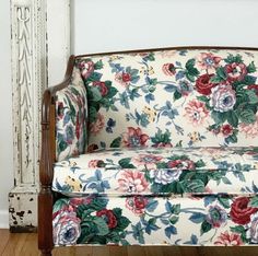 a floral couch sitting on top of a hard wood floor next to a white wall