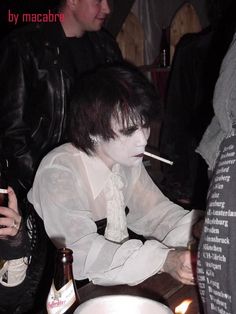 a man with white paint on his face sitting at a table next to a candle