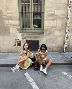 two young women sitting on the ground next to each other holding cell phones in their hands