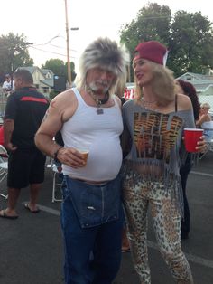 a man and woman standing next to each other in a parking lot with people around them