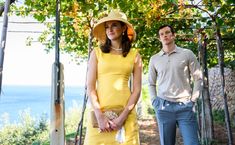 a woman in a yellow dress and hat standing next to a man wearing blue pants