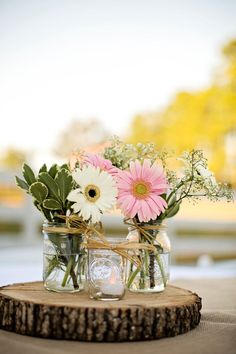 mason jars filled with flowers are sitting on a tree stump