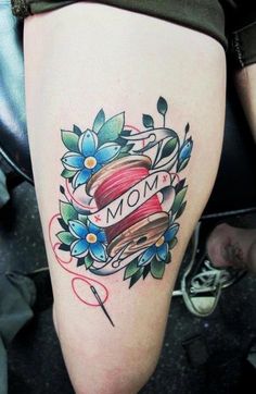 a tattoo on the leg of a woman with a spool of thread and flowers