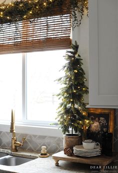 a christmas tree in the corner of a kitchen window sill with lights on it