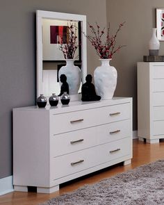 a white dresser with two vases on top of it next to a bed in a bedroom