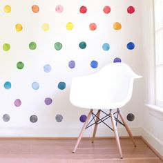 a white chair sitting in front of a wall with multicolored polka dots on it