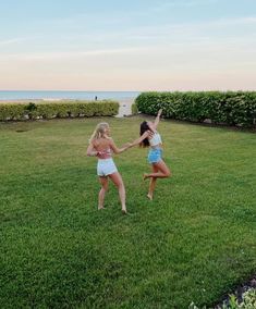 two young women playing with a frisbee in a grassy area near the ocean