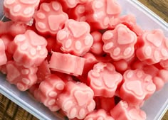 a plastic container filled with lots of pink gummy bear candies on top of a wooden table