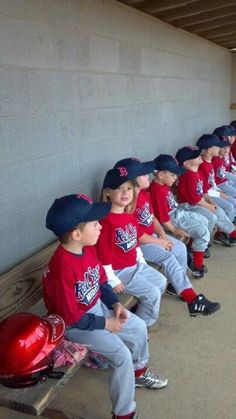 a group of little league baseball players sitting next to each other in the dugout