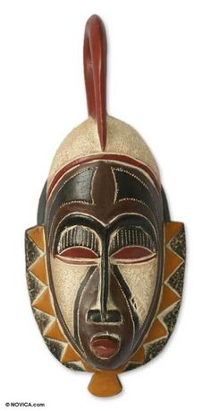 an african mask hanging from the side of a white wall with a brown and red design on it