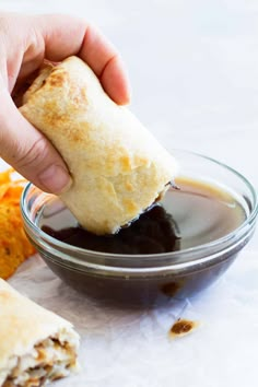 a person dipping some food into a bowl with sauce on the side and another hand holding a piece of bread