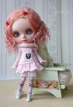 a doll with pink hair is standing next to a white teddy bear on a table