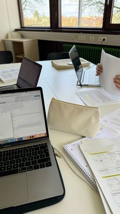 two people sitting at a table with laptops and papers